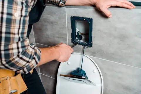 Instalator naprawia spłuczkę, używając narzędzi do regulacji mechanizmu.